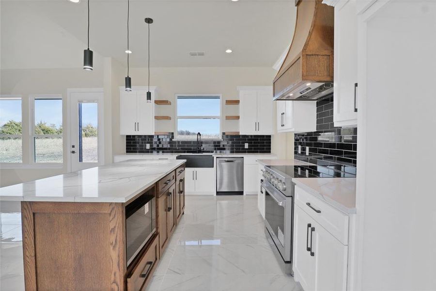 Kitchen featuring sink, stainless steel appliances, light stone countertops, white cabinets, and a kitchen island