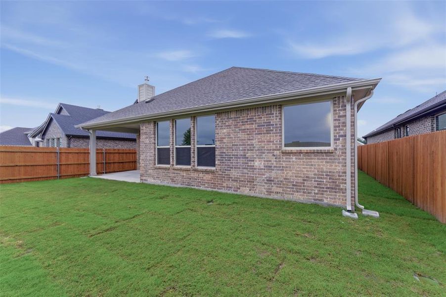Expansive rear yard featuring green lawn, a covered patio, and a privacy fence