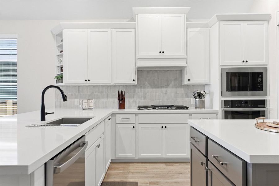 Modern kitchen featuring white shaker cabinetry, light-toned countertops, a stainless steel sink with a matte black faucet, a built-in microwave, and a wall oven