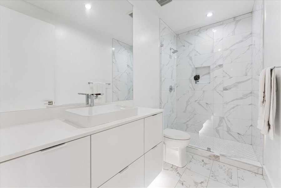Bathroom with vanity, a marble finish shower, light marble finish flooring, and recessed lighting