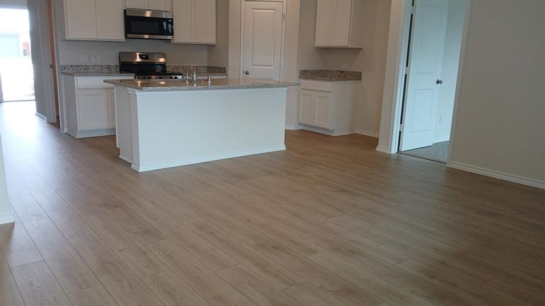 Open-concept kitchen and living area featuring wood-finish flooring, white cabinetry, granite countertops, and stainless steel appliances including a range and microwave Open-concept kitchen and living area featuring wood-finish flooring, white cabinetry, granite countertops, and stainless steel appliances including a range and microwave