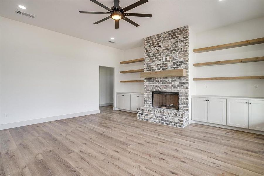 Unfurnished living room with a brick fireplace, light hardwood / wood-style flooring, and ceiling fan