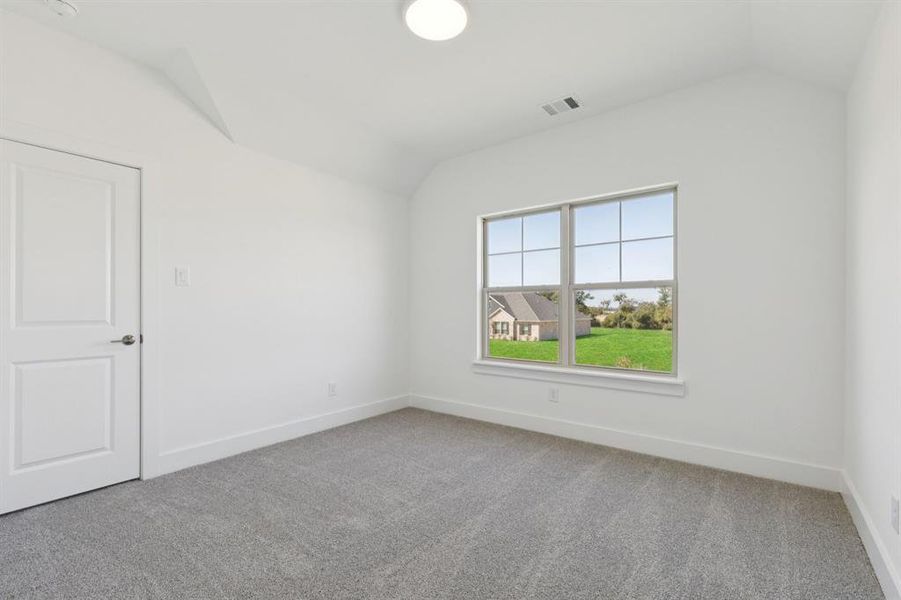 Empty room with vaulted ceiling and light carpet