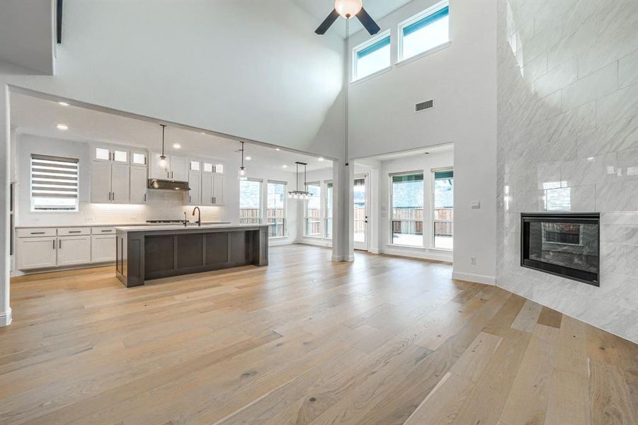 Kitchen with visible vents, light wood finished floors, under cabinet range hood, a tiled fireplace, and open floor plan