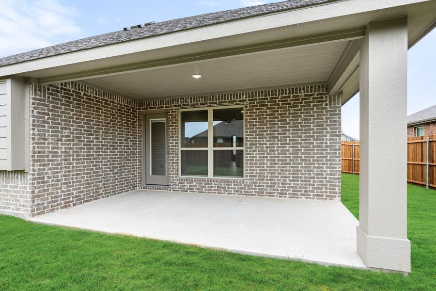Covered back patio with concrete floor, brick exterior wall, and fenced backyard with green lawn