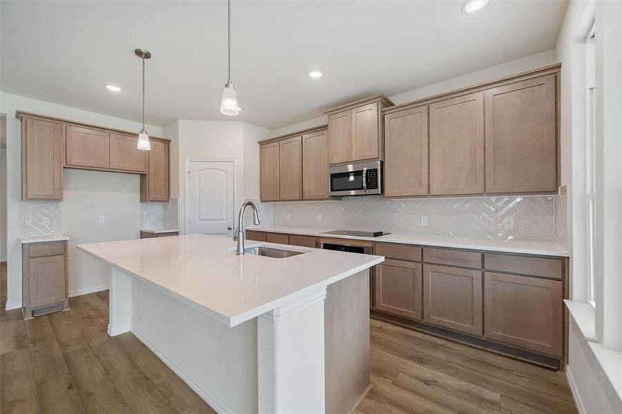 Kitchen featuring decorative backsplash, light stone counters, stainless steel microwave, light wood-style floors, and pendant lighting