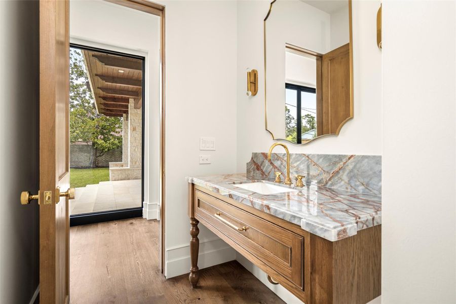 A refined powder room pairs a furniture-style white oak vanity with richly veined natural stone, warm brass fixtures, and a graceful framed mirror. Direct access to the outdoor living area makes it as functional as it is beautifully appointed. A refined powder room pairs a furniture-style white oak vanity with richly veined natural stone, warm brass fixtures, and a graceful framed mirror. Direct access to the outdoor living area makes it as functional as it is beautifully appointed.