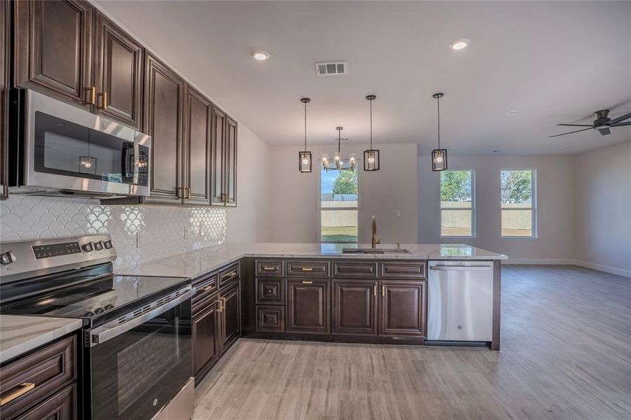 Kitchen featuring light hardwood / wood-style flooring, hanging light fixtures, kitchen peninsula, sink, and appliances with stainless steel finishes