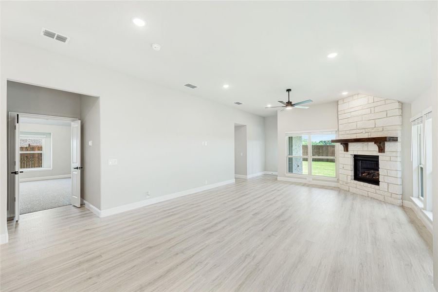 Open living room with light wood floors, stone fireplace, and ceiling fan