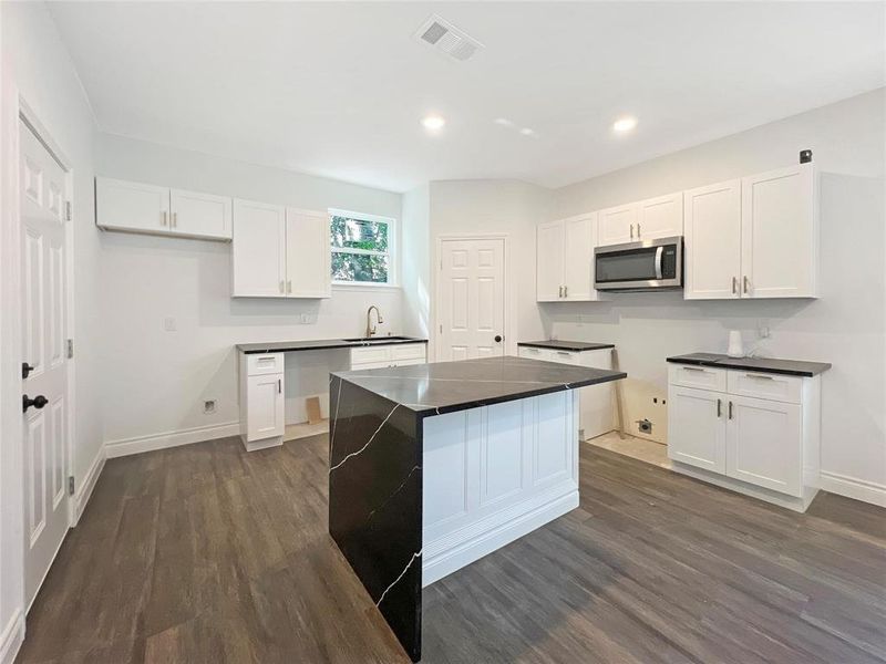 Kitchen featuring dark wood-style floors, white cabinetry, stainless steel microwave, a kitchen island, and recessed lighting Kitchen featuring dark wood-style floors, white cabinetry, stainless steel microwave, a kitchen island, and recessed lighting