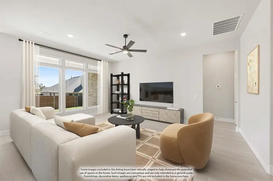 Living room with sectional sofa, ceiling fan, wall-mounted TV, and large windows with backyard view