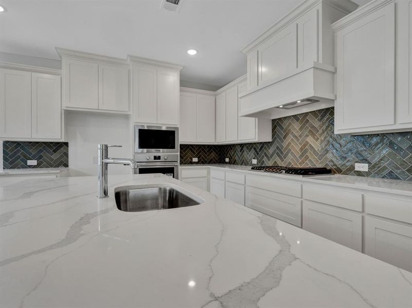 Kitchen with decorative backsplash, light stone countertops, stainless steel appliances, and white cabinetry