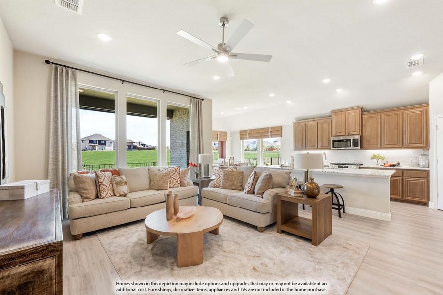 Open-concept living room with two sofas and ceiling fan, flowing into kitchen with wood cabinets and island