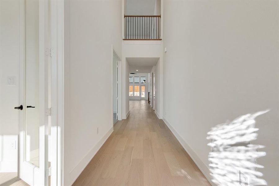 Hall featuring light wood-style flooring and a towering ceiling