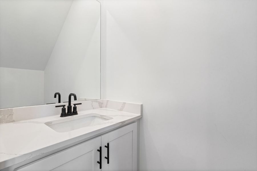 White vanity with panel doors, black hardware, integrated rectangular sink, black faucet, and a large wall-mounted mirror White vanity with panel doors, black hardware, integrated rectangular sink, black faucet, and a large wall-mounted mirror