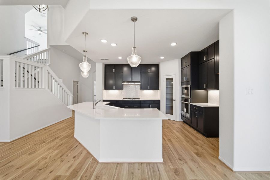 Kitchen with dark cabinetry, tasteful backsplash, pendant lighting, light wood-style flooring, and stainless steel appliances