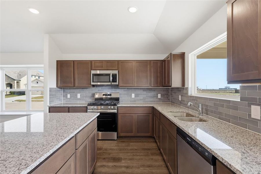 Kitchen with stainless steel appliances, light stone counters, dark wood-style flooring, tasteful backsplash, and recessed lighting Kitchen with stainless steel appliances, light stone counters, dark wood-style flooring, tasteful backsplash, and recessed lighting