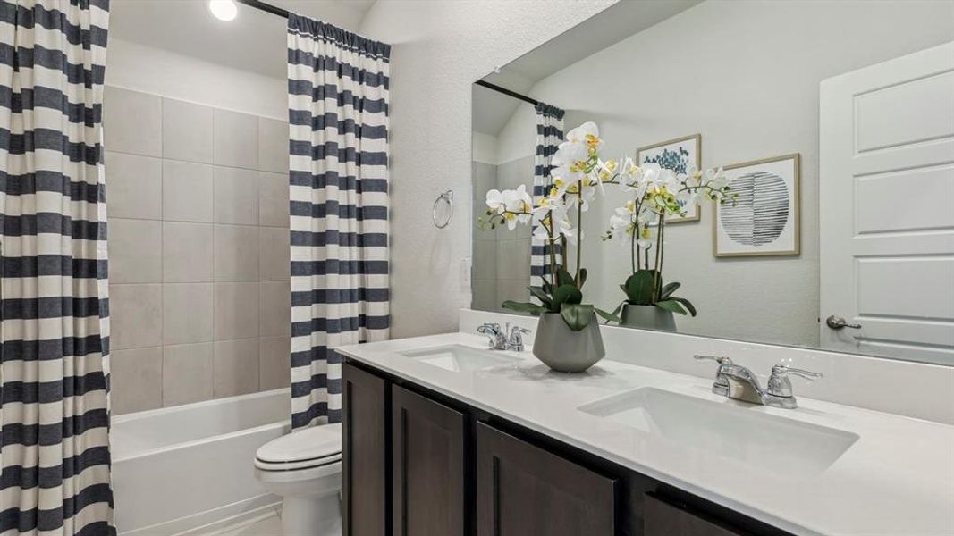 Bathroom featuring a double vanity with two sinks and a spacious mirror, a toilet, and a bathtub with tiled surround