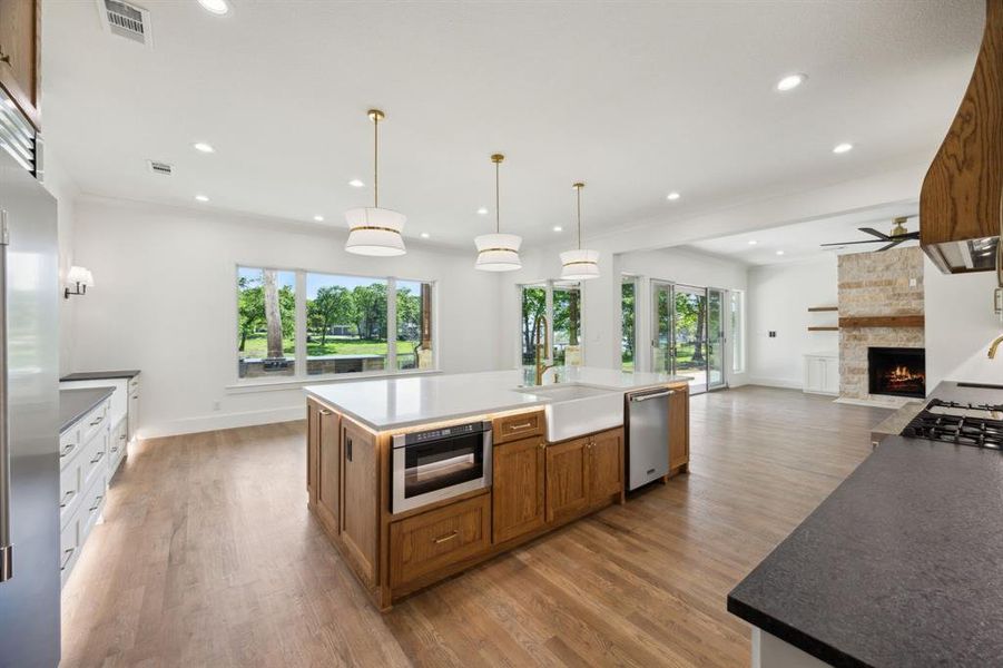 Kitchen featuring a stone fireplace, visible vents, brown cabinetry, dishwasher, and a sink Kitchen featuring a stone fireplace, visible vents, brown cabinetry, dishwasher, and a sink