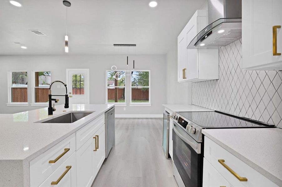 Kitchen featuring pendant lighting, white cabinets, sink, wall chimney exhaust hood, and appliances with stainless steel finishes