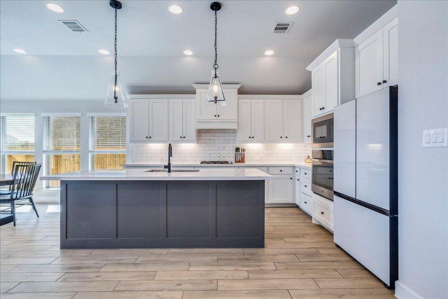 Kitchen featuring stainless steel appliances, dual tone cabinetry, hanging light fixtures, a kitchen island with sink, and light wood-type flooring