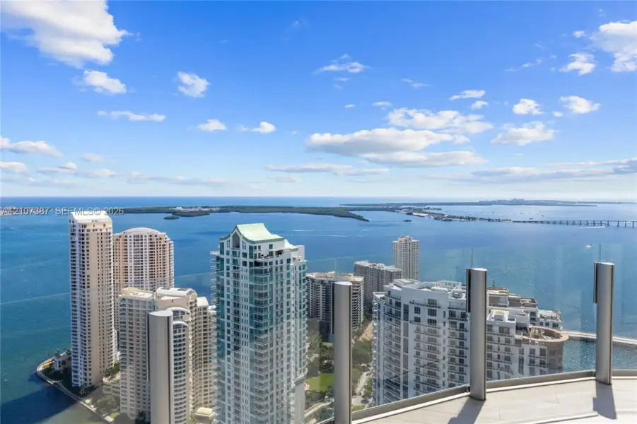 High-floor balcony with glass panel railing and tile flooring overlooking a bay and surrounding urban skyline