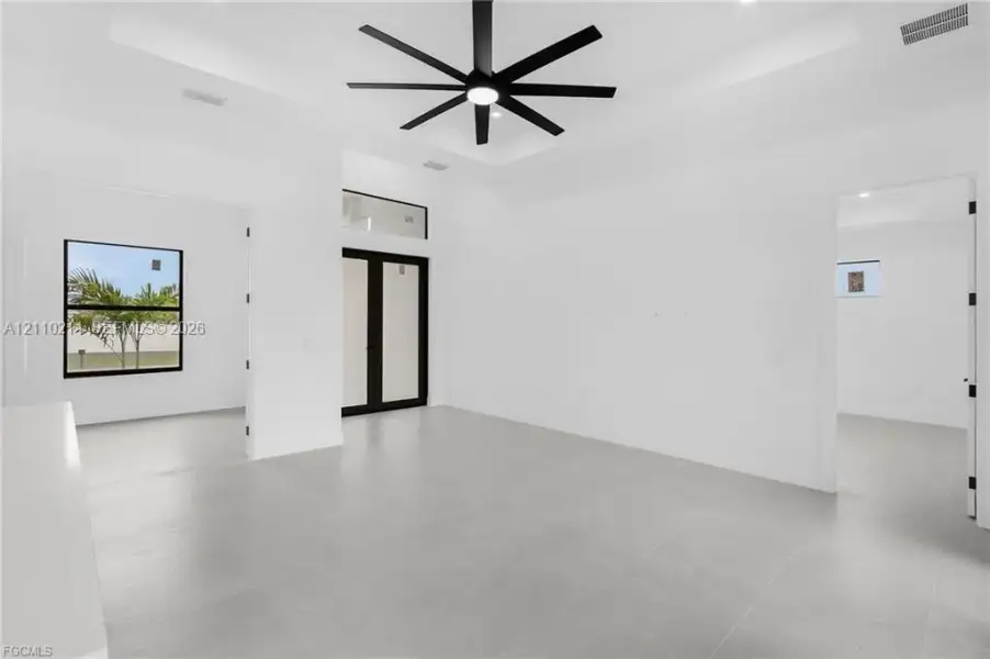 Tray ceiling, large-format tile flooring, matte black multi-blade ceiling fan, and black-framed glass entry doors with transom window