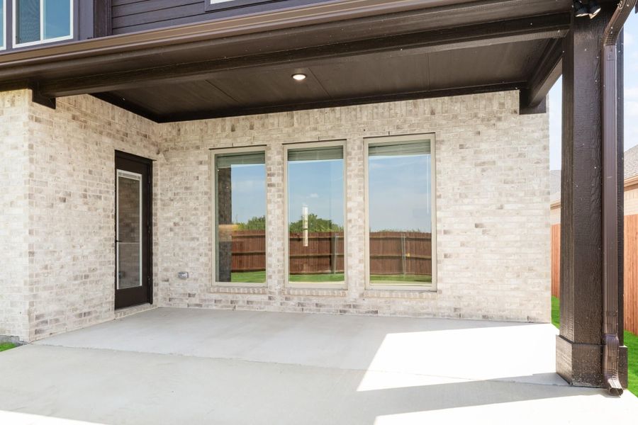 Covered back patio with concrete floor, light brick exterior, three windows, and a back door