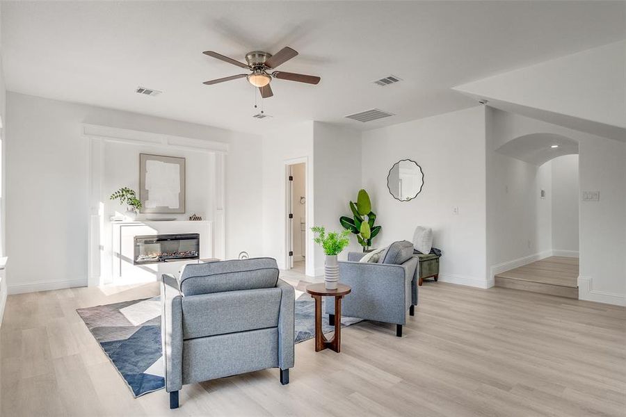 Living room featuring light wood-style floors, a glass covered fireplace, ceiling fan, and arched walkways Living room featuring light wood-style floors, a glass covered fireplace, ceiling fan, and arched walkways