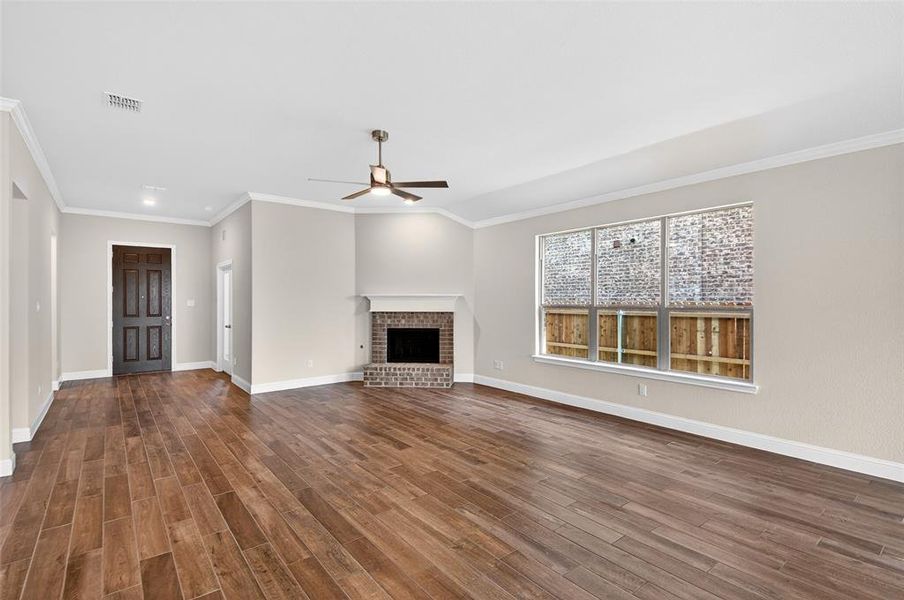Spacious living area featuring wood-finish flooring, a brick fireplace with a white mantel, and a ceiling fan with integrated lighting