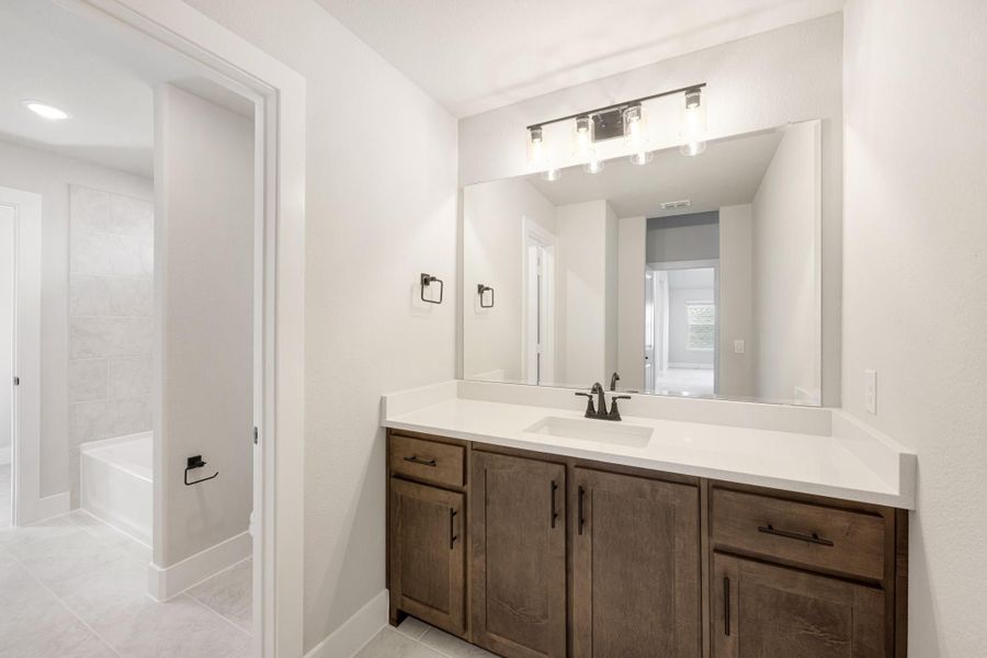 Bathroom vanity with dark wood cabinets, white countertop, large mirror, and view of tiled tub area Bathroom vanity with dark wood cabinets, white countertop, large mirror, and view of tiled tub area