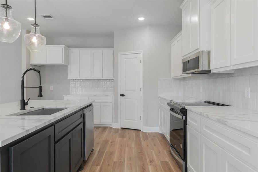 Kitchen with white cabinetry, backsplash, light wood-type flooring, and stainless steel appliances