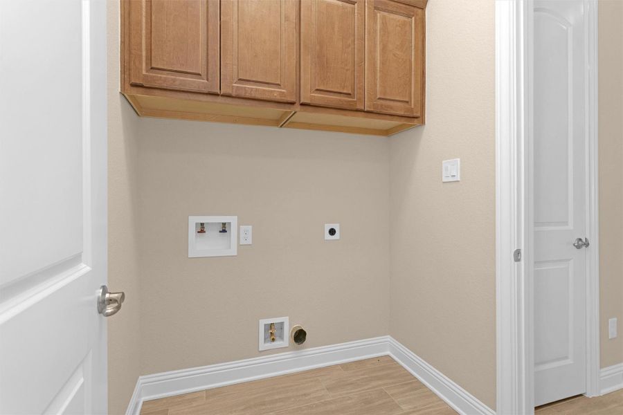 This laundry room offers upper cabinetry for extra storage, washer and dryer hookups, and easy-to-clean wood-look tile flooring in a clean, functional layout.