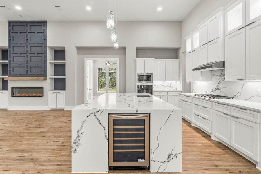 A showpiece kitchen featuring a dramatic waterfall island, built-in wine fridge, soaring cabinetry, and designer lighting.