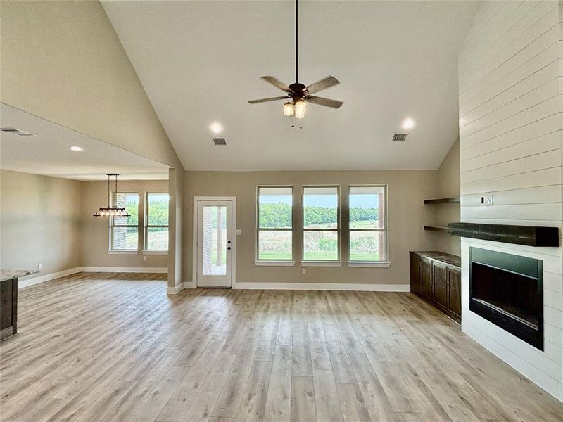 Unfurnished living room featuring a fireplace, plenty of natural light, high vaulted ceiling, light wood-type flooring, and a ceiling fan Unfurnished living room featuring a fireplace, plenty of natural light, high vaulted ceiling, light wood-type flooring, and a ceiling fan