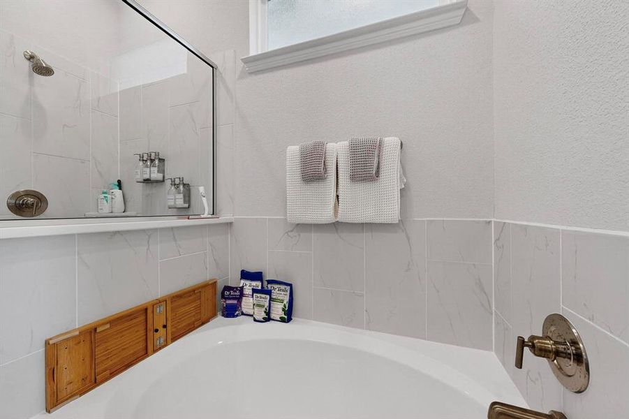 Full bath featuring a bath, a shower, and a textured wall Full bath featuring a bath, a shower, and a textured wall