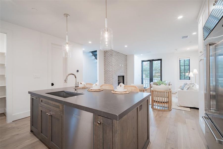 Kitchen featuring decorative light fixtures, sink, light hardwood / wood-style floors, dark brown cabinets, and a center island with sink