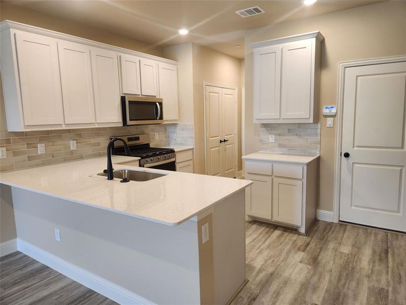 Kitchen with appliances with stainless steel finishes, tasteful backsplash, light hardwood / wood-style floors, and white cabinetry