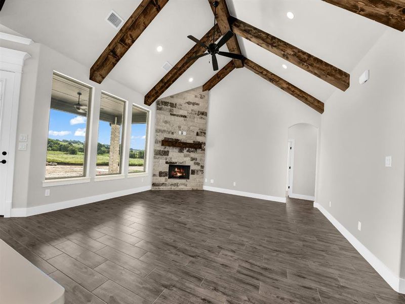 Unfurnished living room with high vaulted ceiling, a stone fireplace, ceiling fan, dark wood finished floors, and beamed ceiling