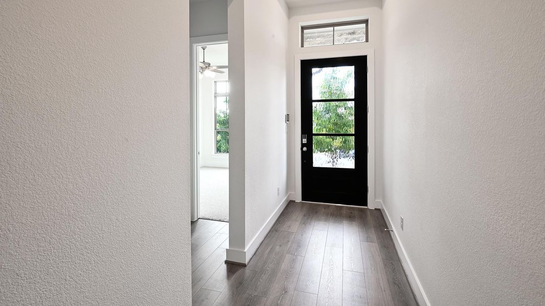 Foyer entrance featuring a textured wall, dark wood-type flooring, and ceiling fan Foyer entrance featuring a textured wall, dark wood-type flooring, and ceiling fan