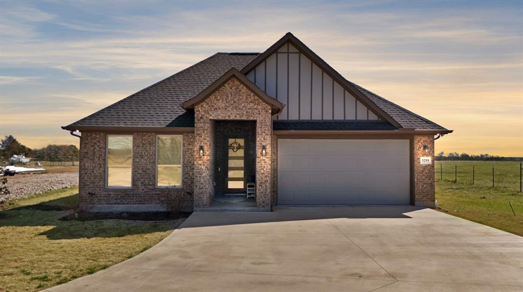 View of front of house with a shingled roof, an attached garage, board and batten siding, fence, and driveway