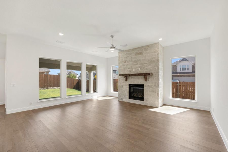 Open living room with stone fireplace, wood mantel, hardwood floors, and ceiling fan