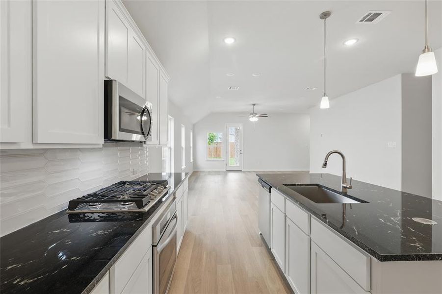 Kitchen featuring white cabinetry, light wood-style floors, a kitchen island with sink, dark stone countertops, and lofted ceiling