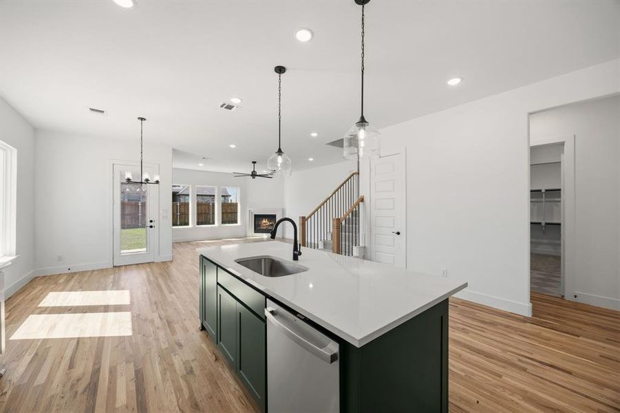 Kitchen featuring green cabinets, dishwasher, a lit fireplace, a chandelier, and an island with sink