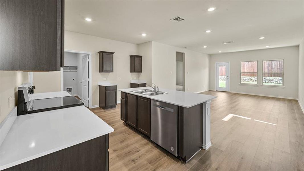 Open-concept kitchen featuring dark wood-finish cabinetry, light countertops, and stainless steel appliances