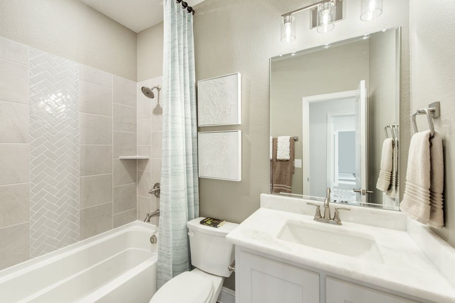 Bathroom with white vanity, tub-shower combo with herringbone tile, and large mirror with overhead lighting