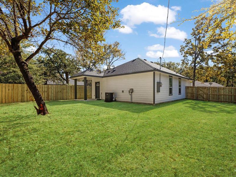 Rear view of house with a fenced backyard, roof with shingles, and a patio