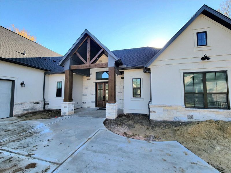 This modern home with a welcoming front entrance, features a gabled roof and wooden beams. The exterior combines stone and light siding, complemented by large windows. The driveway leads to a spacious garage. This modern home with a welcoming front entrance, features a gabled roof and wooden beams. The exterior combines stone and light siding, complemented by large windows. The driveway leads to a spacious garage.