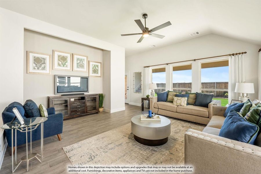 Living room with vaulted ceiling, ceiling fan, hardwood floors, and large windows with backyard view