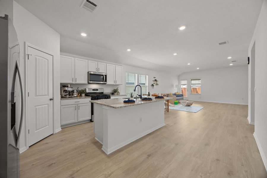 Kitchen with stainless steel appliances, an island with sink, white cabinets, light stone counters, and light wood-type flooring